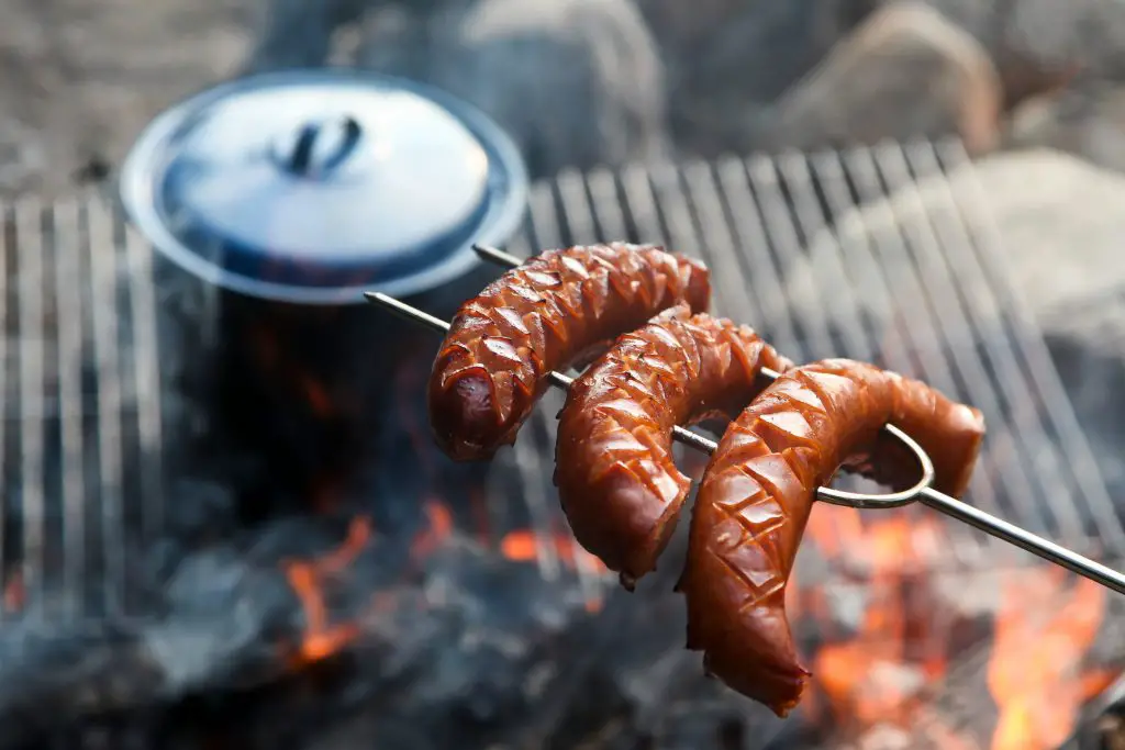 Cooking hot dogs on a fork over a campfire.