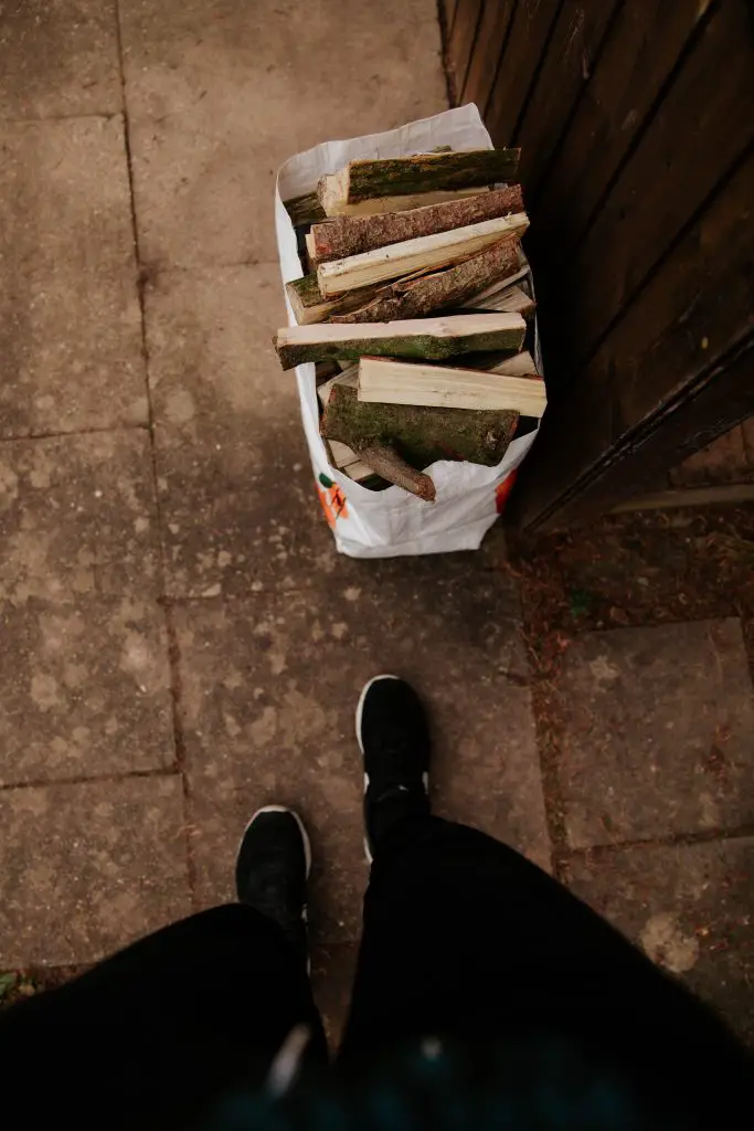 Person's feet standing next to a bag of kindling.