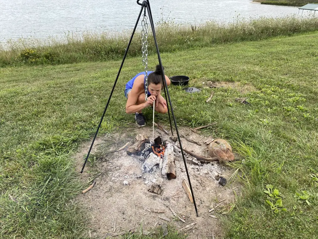 A woman using a campfire bellows to revive a dying campfire