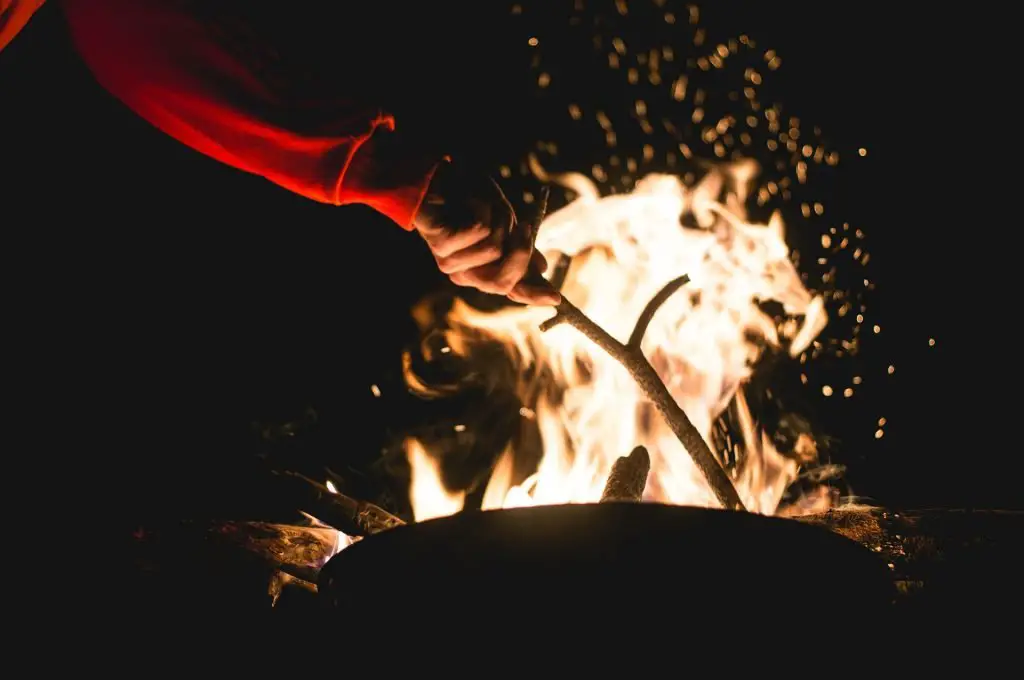 A person stoking a campfire with a stick at night
