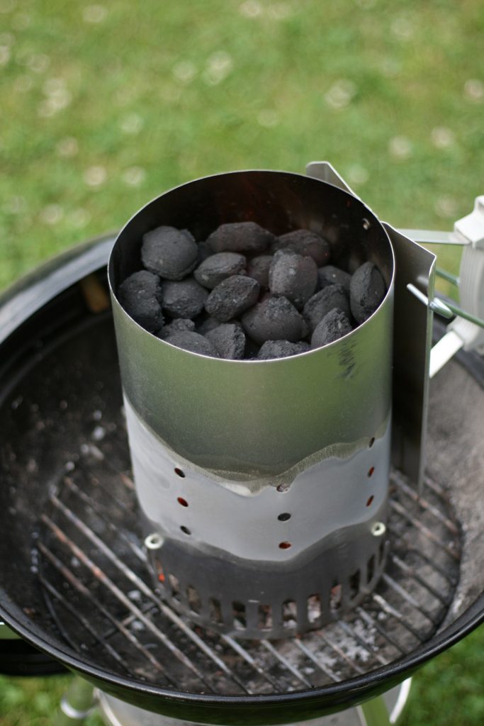 Chimney starter full of briquettes on a kettle grill