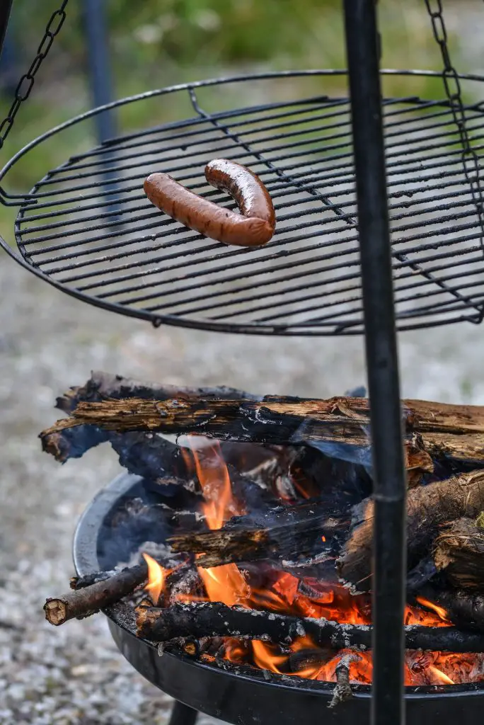 Grill grate hanging from a campfire tripod cooking hot dogs