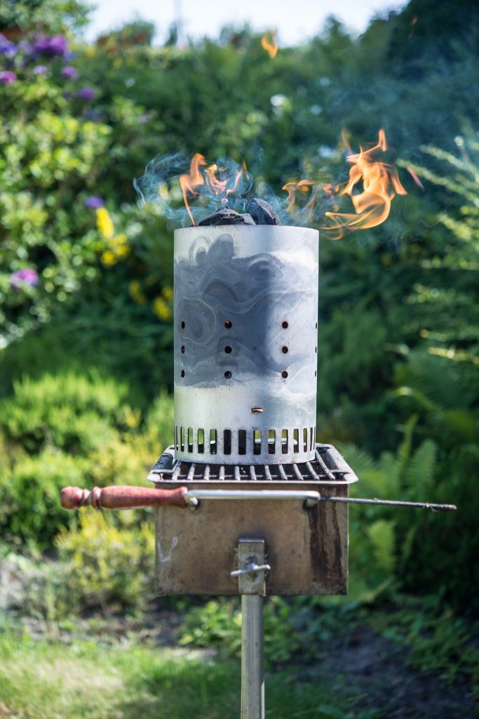 Chimney starter with burning coals sitting on a campsite grill
