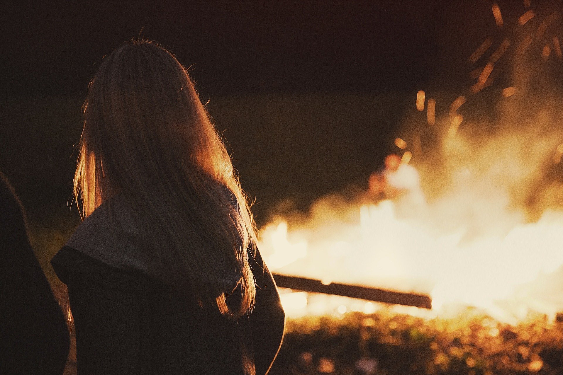 girl standing in front of a campfire at night