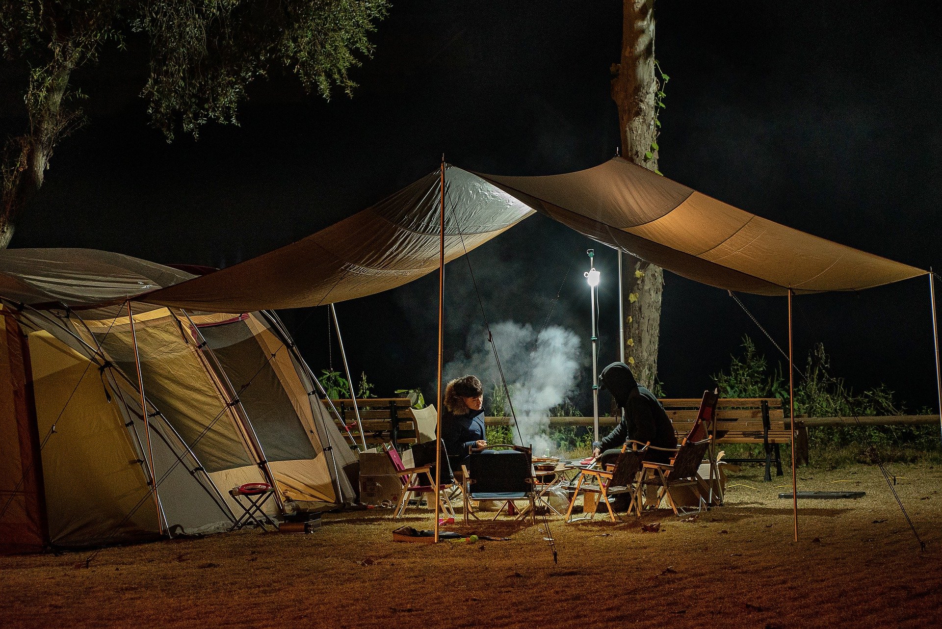 people sitting under a canopy by a campfire