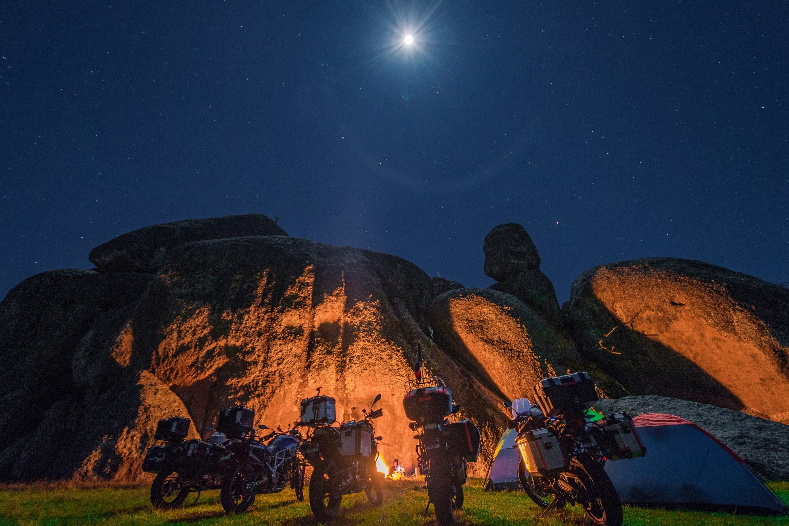 People camping by a boulder using it as a fire reflector
