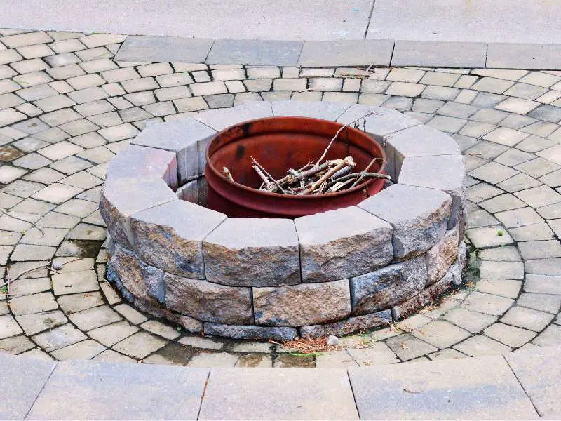 a stone fire pit with a metal bucket full of kindling inside